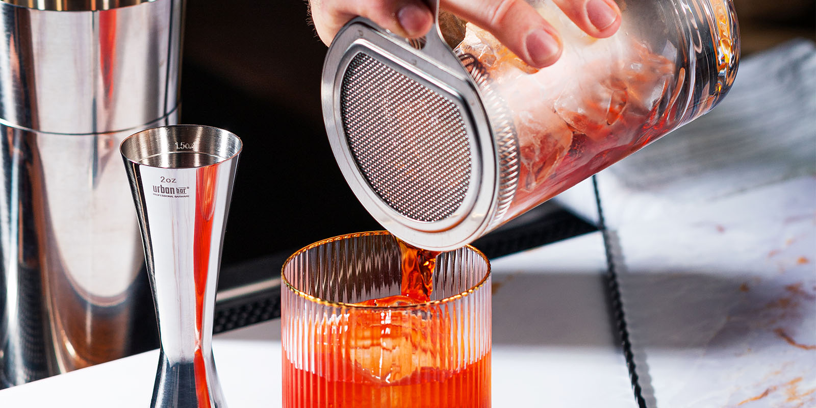 Cocktail being poured from mixing glass into tumbler